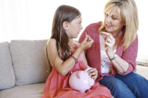 women and money, children; older woman talking about money with a little girl holding a piggy bank