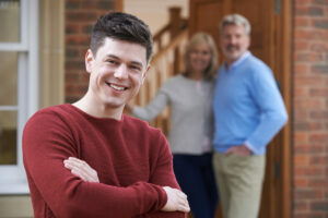 boomerang kids; boomerang kid standing in front of his parents house looking smug