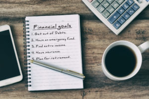 notepad with general financial goals next to a smartphone, calculator, and cup of coffee