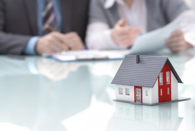 how do mortgages work?; Businessman signs contract behind home architectural model