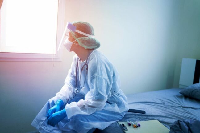 healthcare workers financial relief guide; doctor in PPE looking out a window