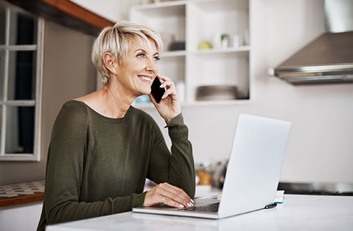 Baby boomer mother at home on the phone and her computer