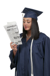 recession guide for grads; woman in cap and gown looking at newspaper classifieds section