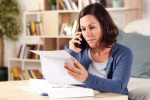 Middle aged woman reviewing her bills while talking on the phone