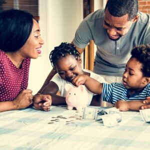 money saving tips for families; man and woman with two young kids counting money with a piggy bank