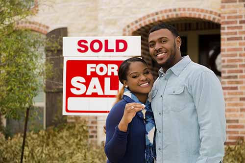 First Time Homebuyers standing in front of a sold house