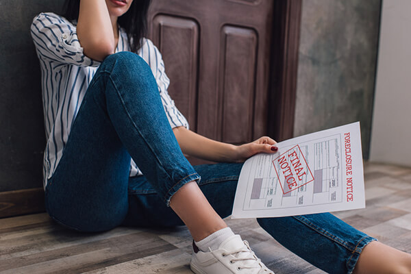 Woman sitting on the floor with hand over head looking over a foreclosure notice