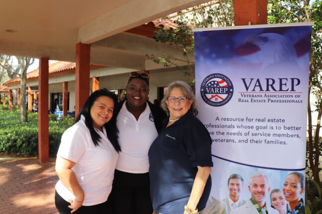 Three people posing together in front of a VAREP banner outdoors